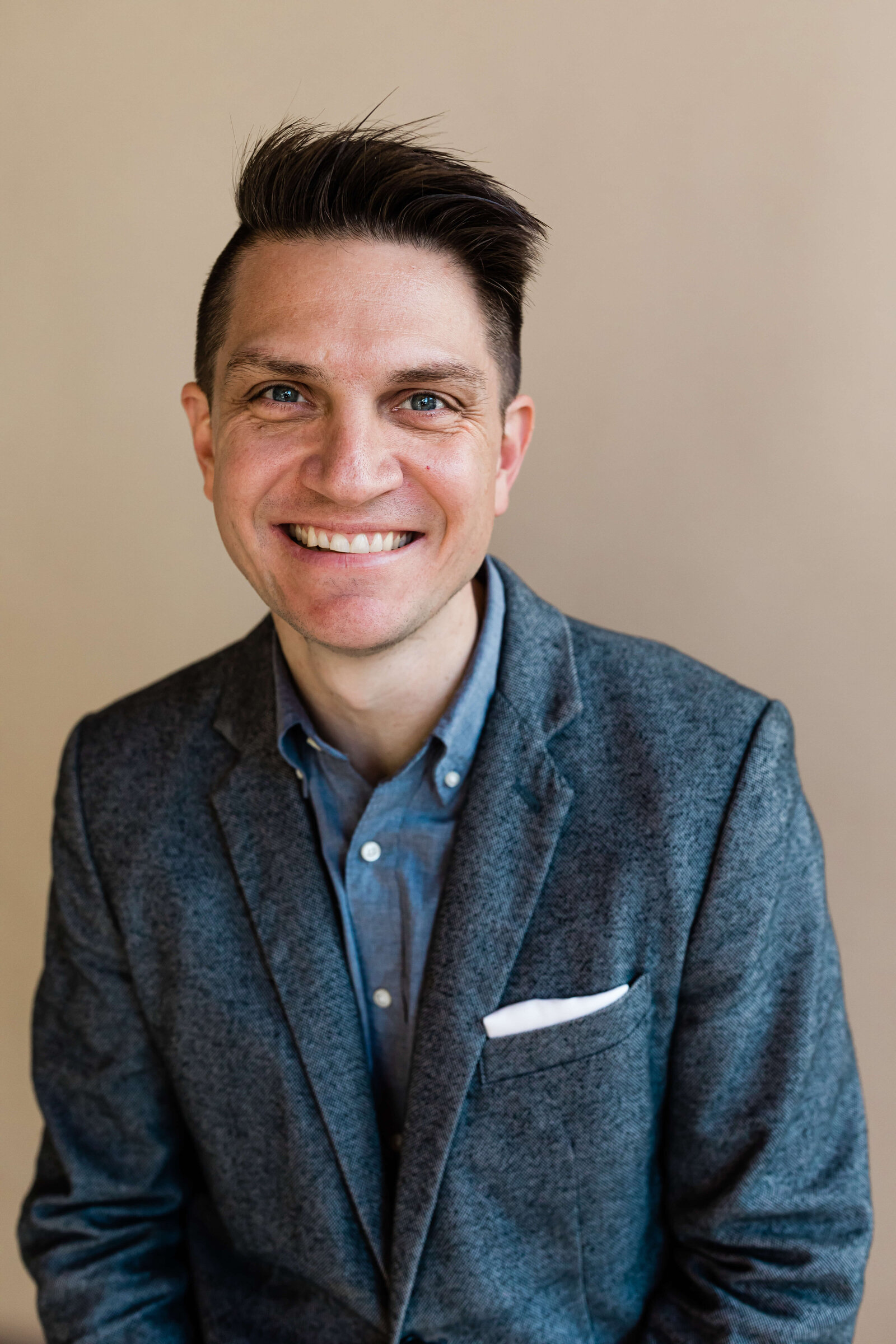 man with short hair cut smiling at camera wearing suit with hankerchief
