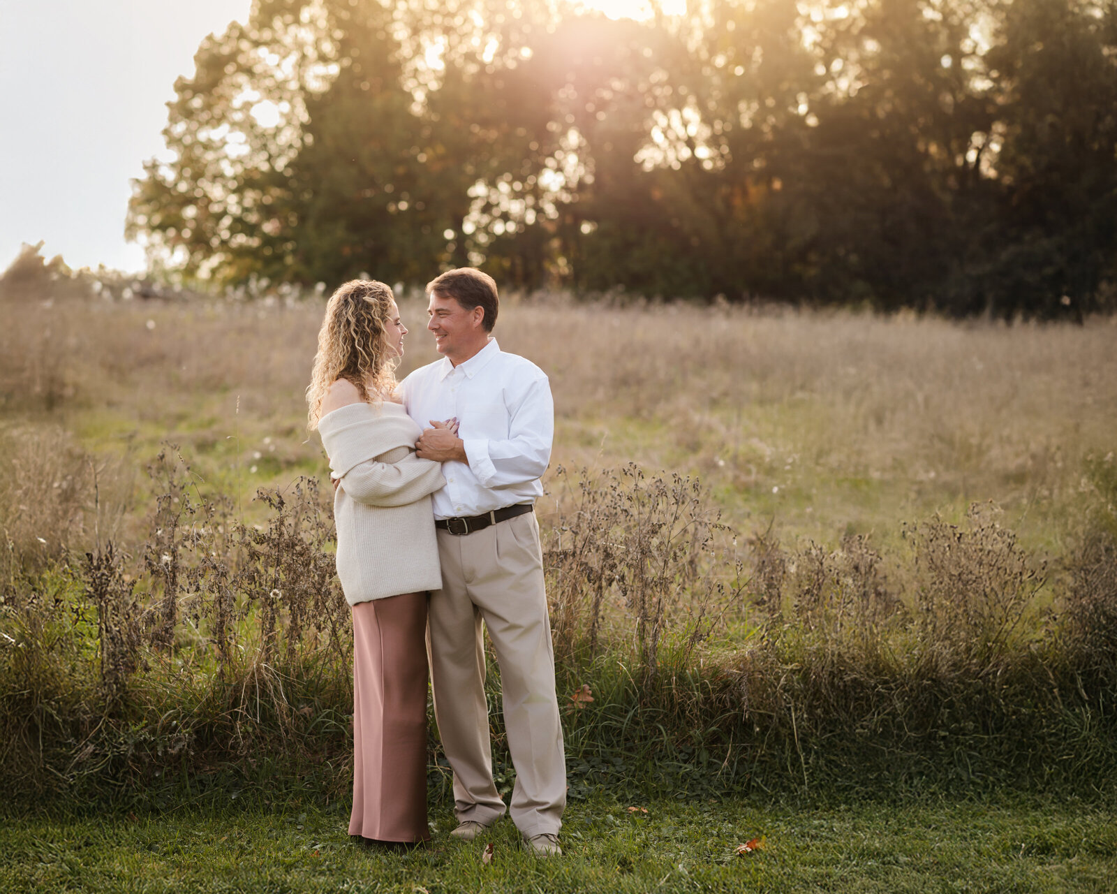 husband and wife hugging for family photos in field at sunset