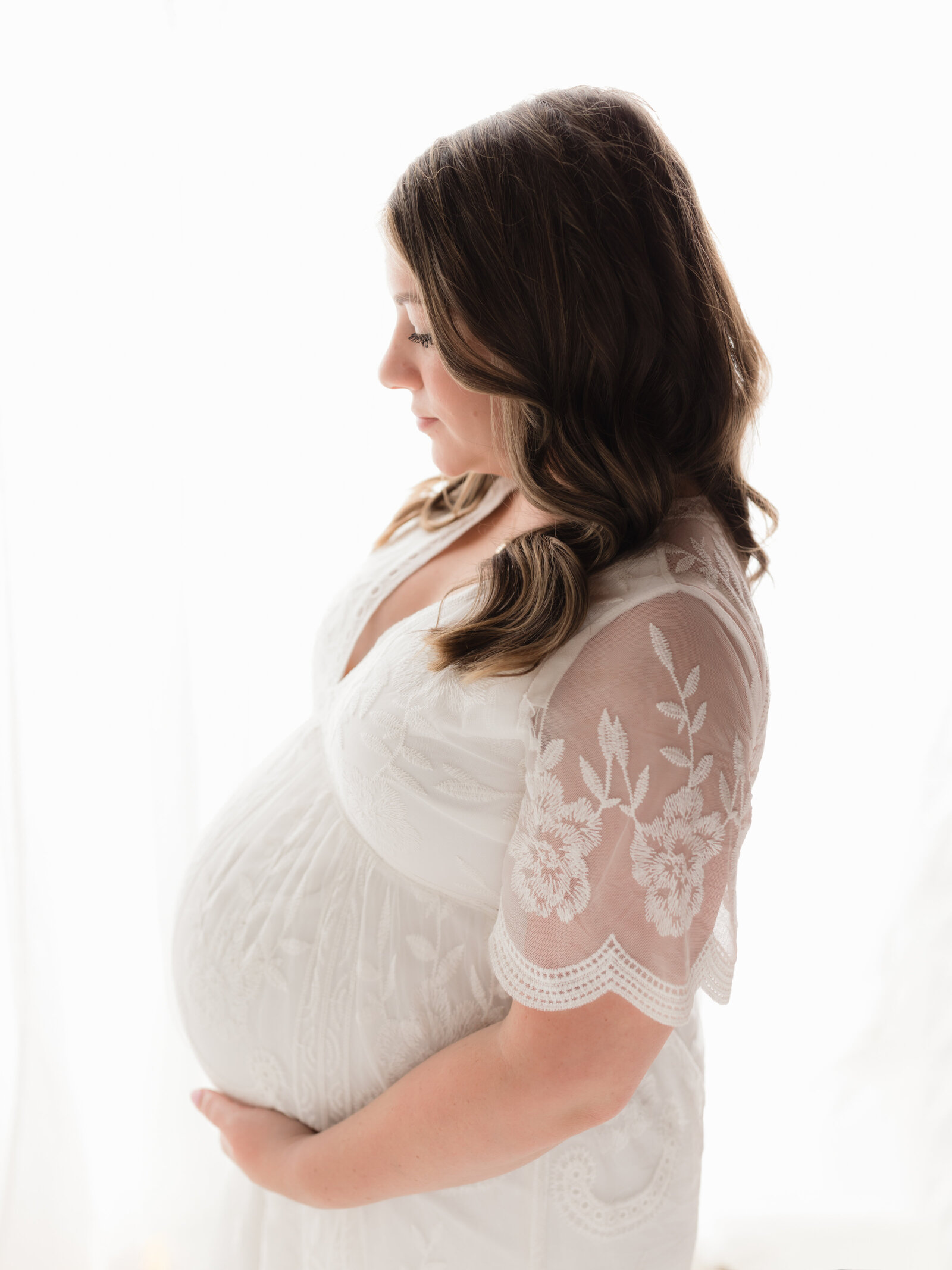 pregnant mother holding belly wearing white lace dress for maternity photoshoot