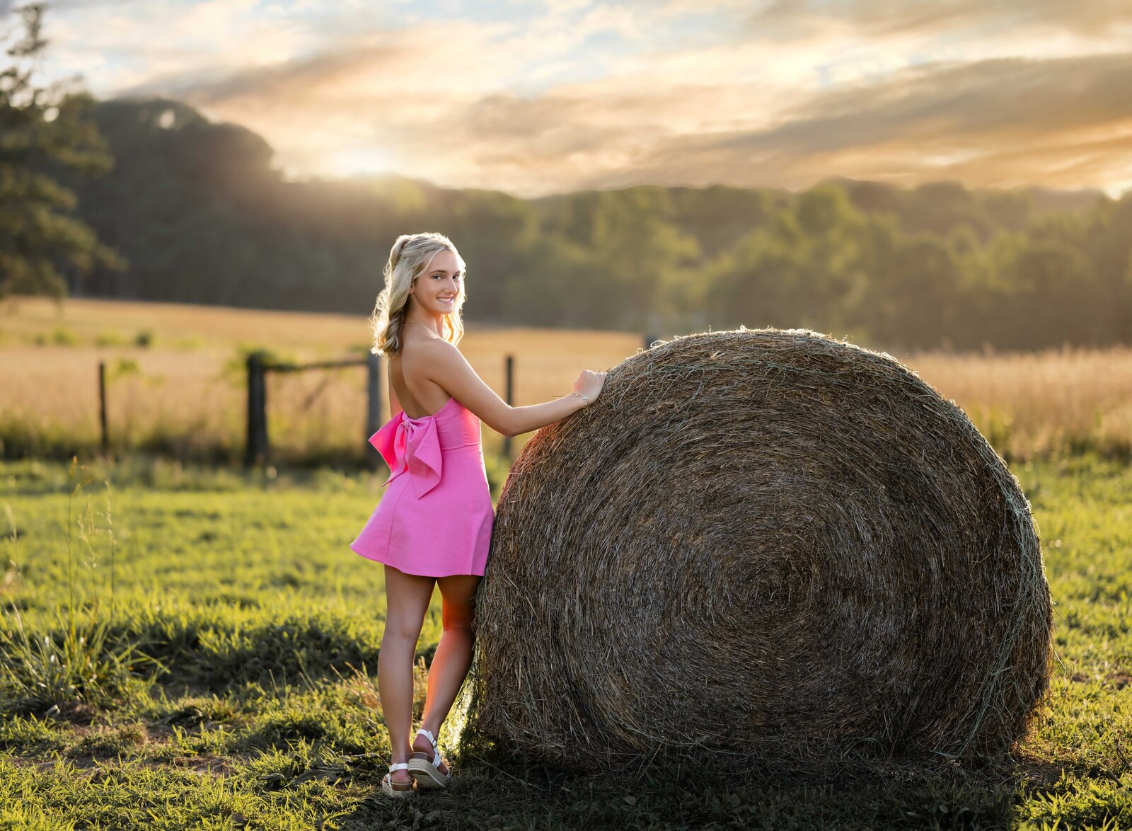 Girl leaning on large hay bale on farm taking senior photos in Atlanta, GA. Graduation photos taken by Jenni Nikki Photography in Atlanta, GA