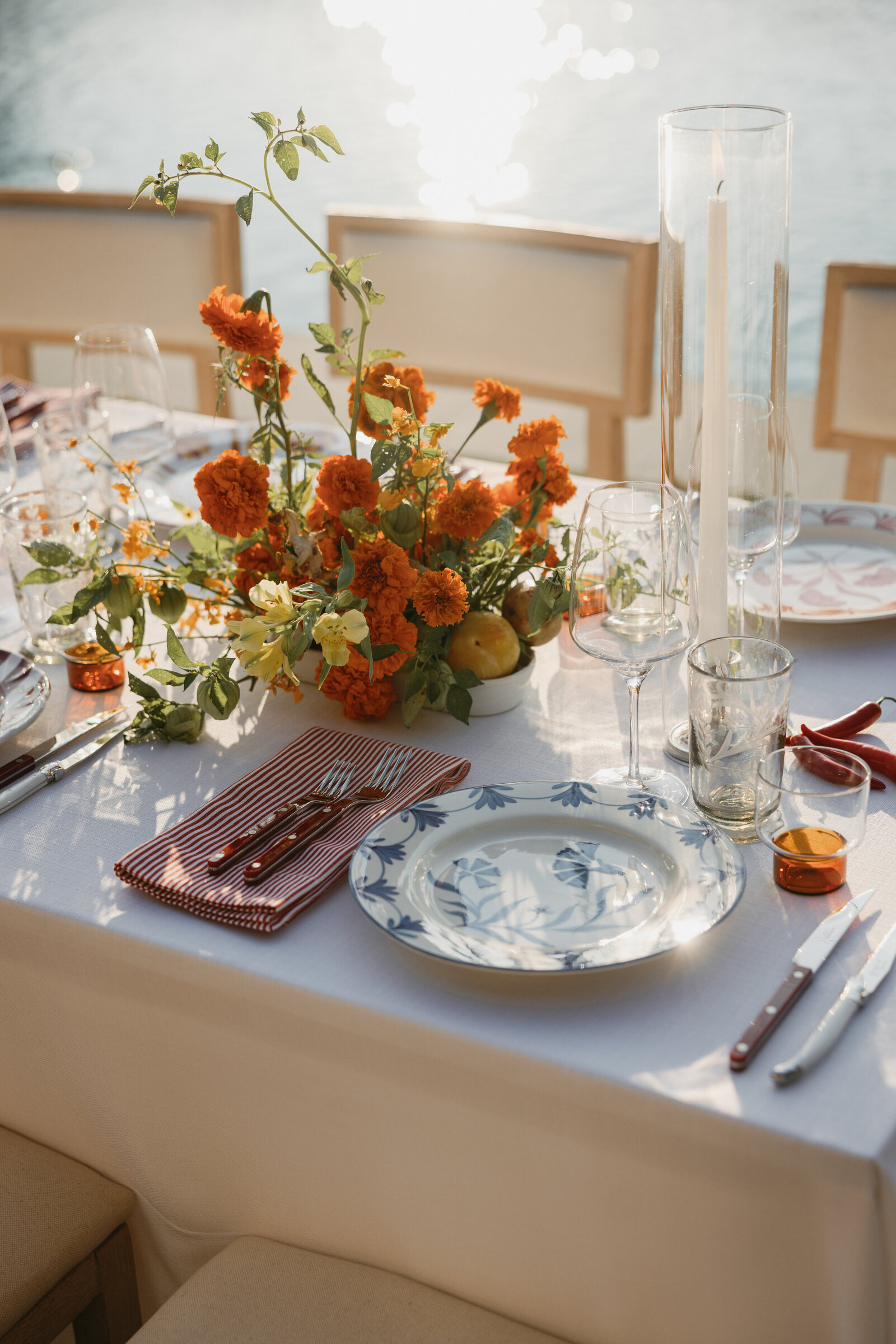 Summer poolside wedding table details with whimsical blue floral plates, red striped napkins, red flatware, and orange & yellow florals
