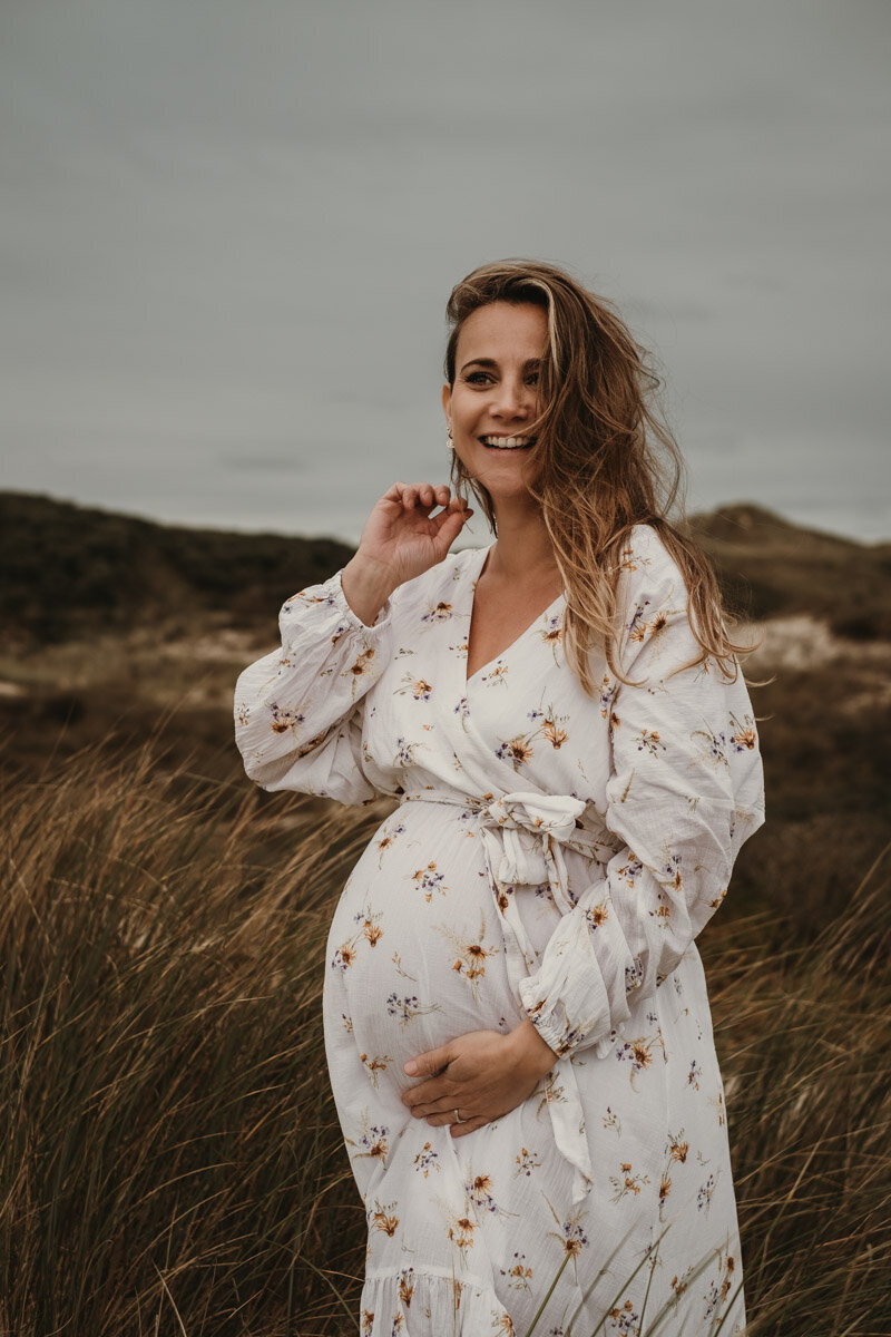 zwangere vrouw in bloemetjesjurk in de duinen
