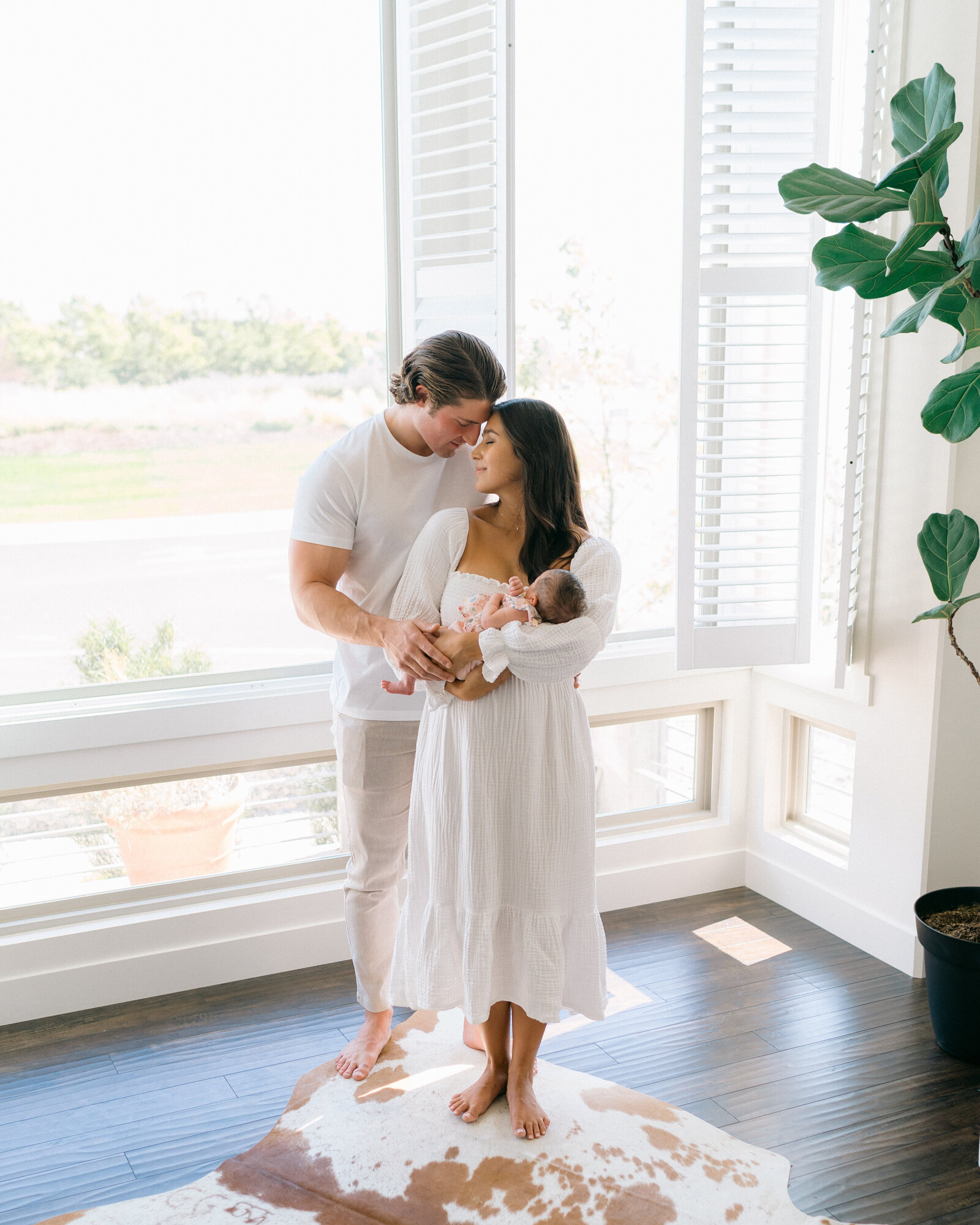 In-home newborn session in Salt Lake City, Utah with beautiful window light – mother holding baby while connecting with dad, captured by a Salt Lake City newborn photographer – soft, intimate family moment in a naturally lit setting.