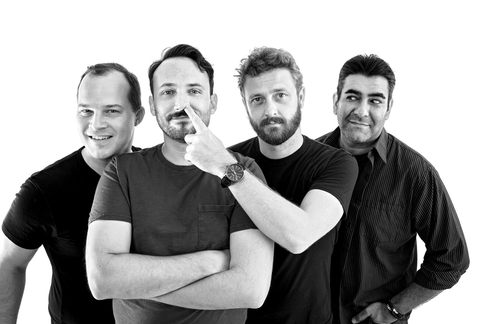 Four men stand together against a white background, exuding energy in this band photography Jacksonville session. One stands front with arms crossed while another playfully points at his face. All appear relaxed, smiling or smirking.