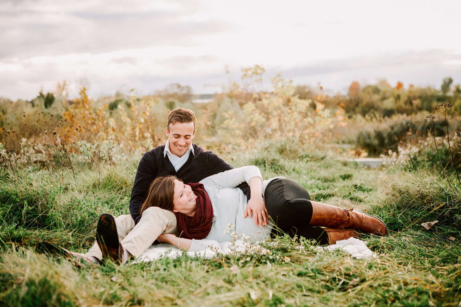 Pregnant couple snuggle in a green field.