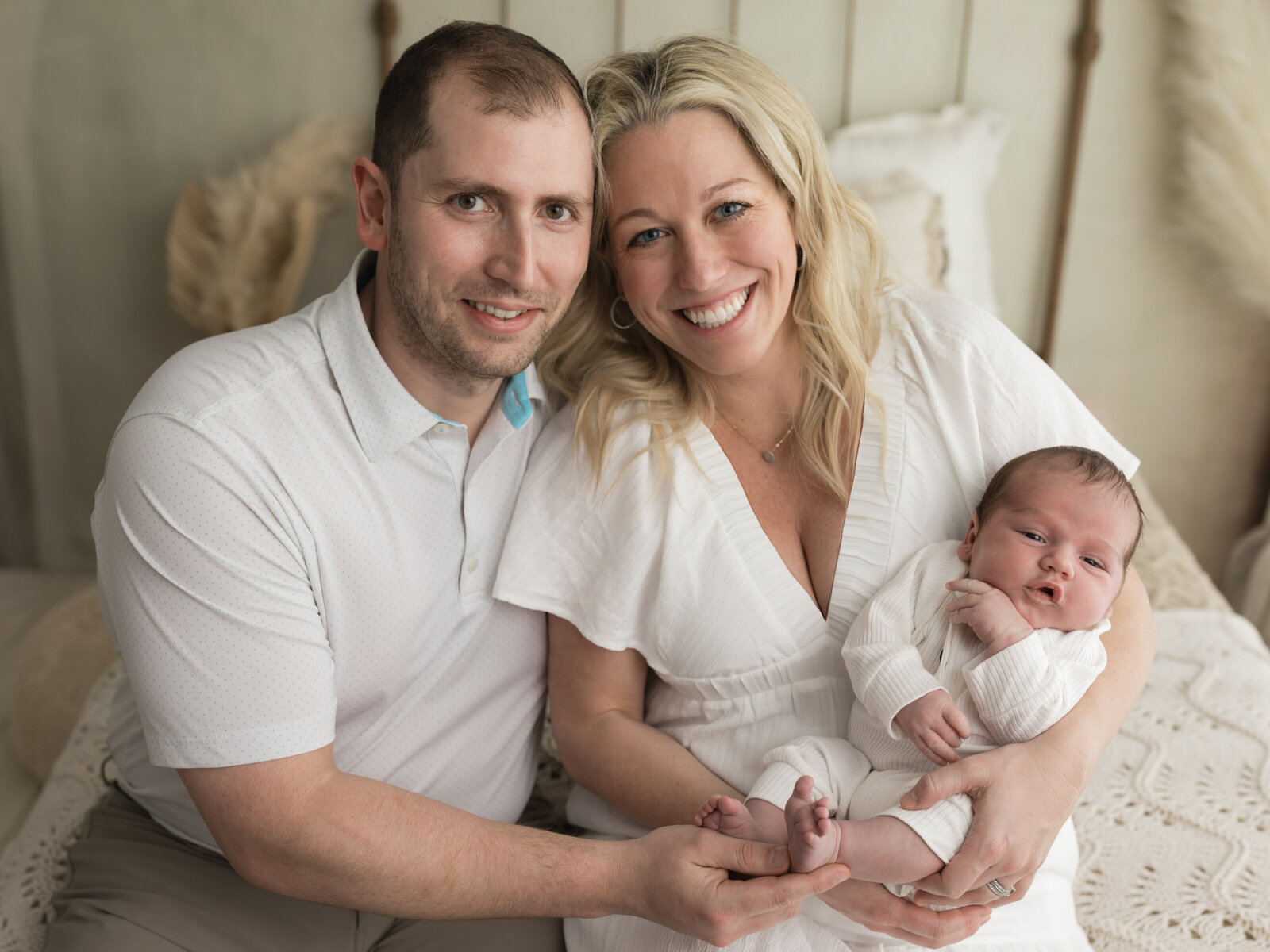 mom and dad holding newborn baby boy in white outfits for studio portraits cleveland newborn photographer