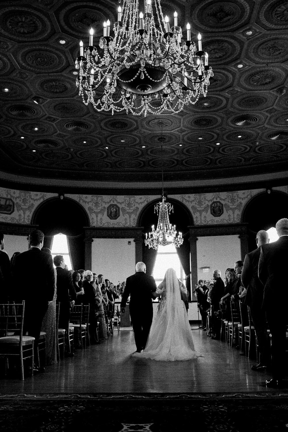 bride and dad down aisle from back with chandelier