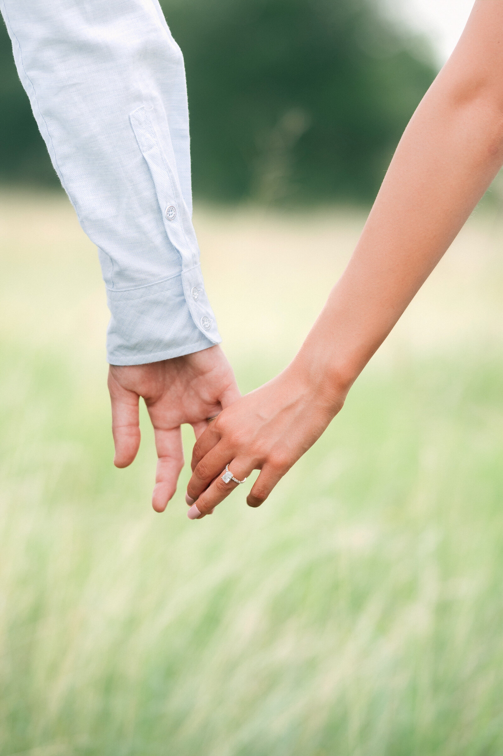 close up of man holding woman's hand in a field in college station tx, woman is wearing engagement ring for engagement session photos