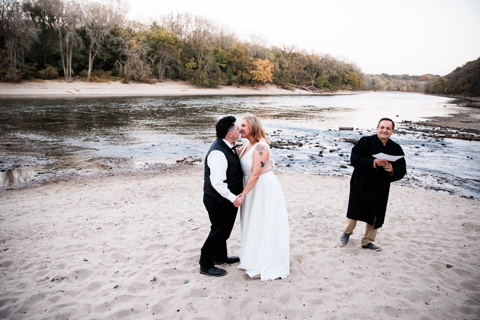 Bride and bride first kiss during an elopement by the Mississippi river bank. 