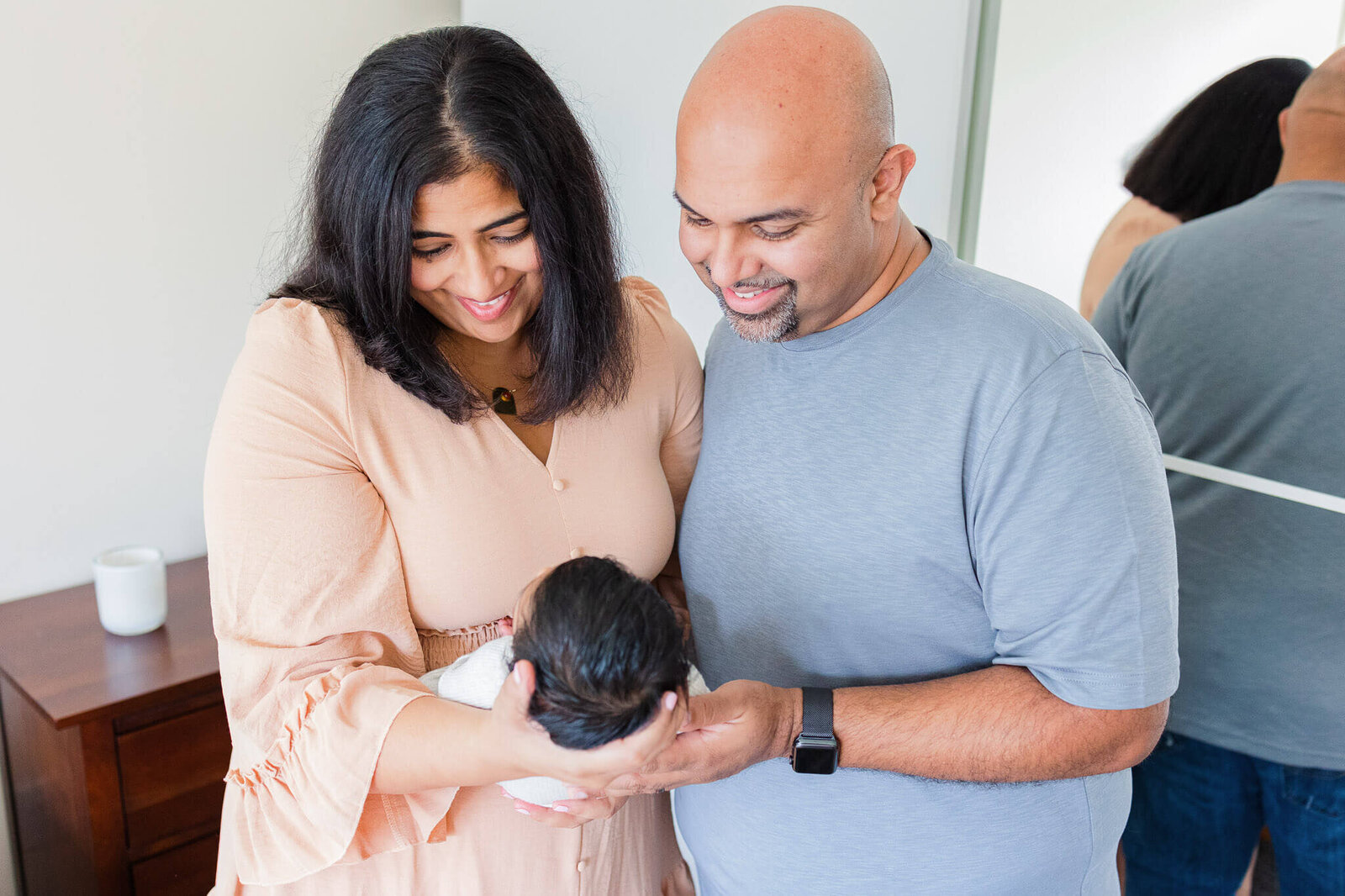 A mom and dad holding their newborn son and smiling down at him.
