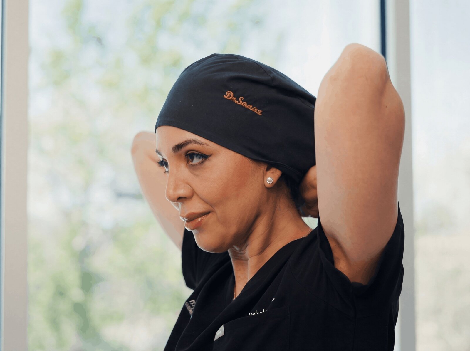 Surgeon tying on a black scrub cap by a window