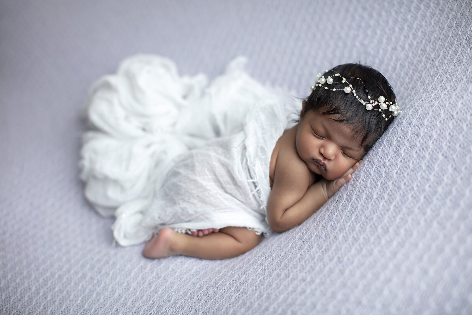 Newborn girl snuggled in purple fabric.