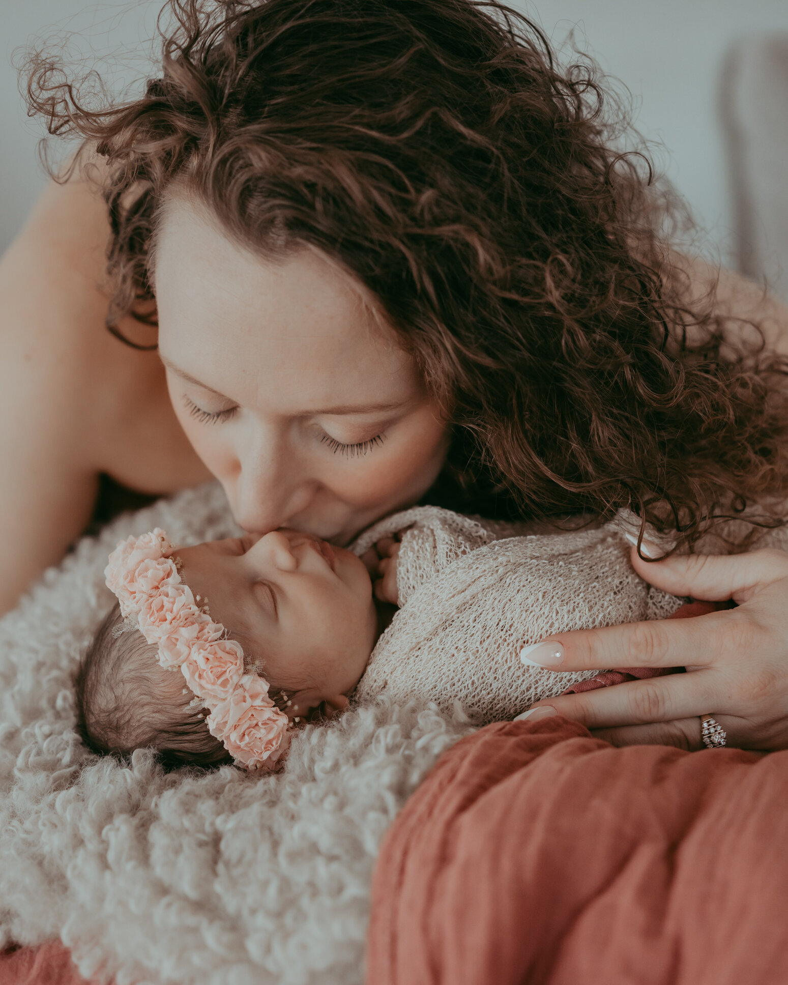 mother kisses her newborn wearing a flower crown