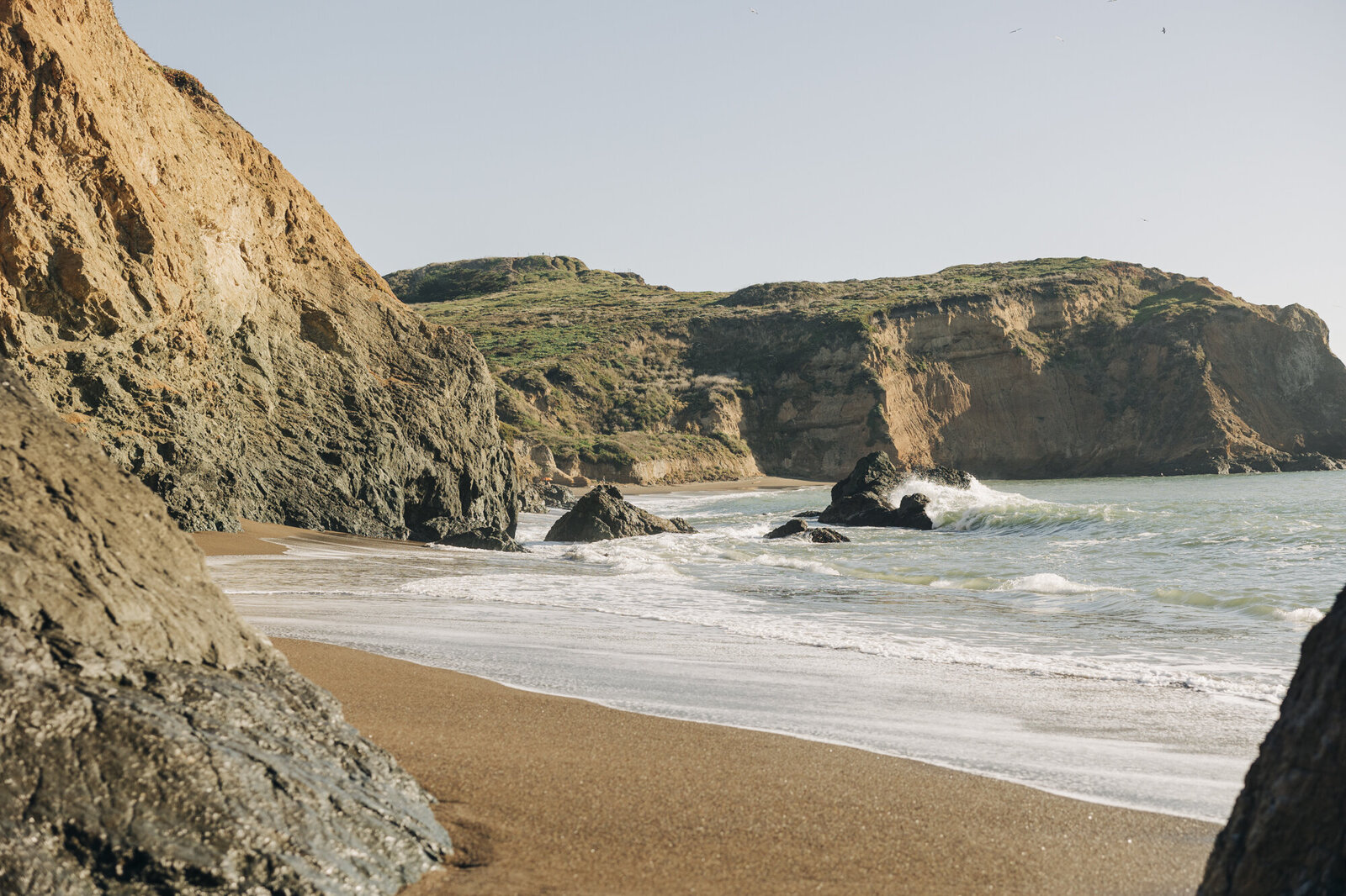 A serene coastline with cliffs and waves gently washing onto a sandy beach, perfect for a destination wedding photographer.