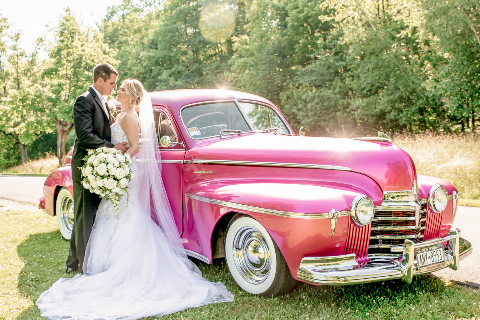 Bride and groom pose in front of a pink classic car