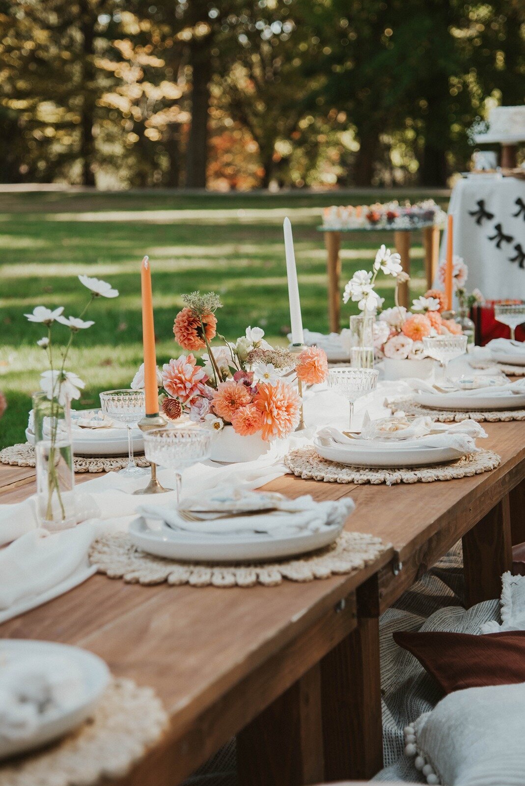 Wooden picnic table decorated with orange and white florals, taper candles, and elegant table settings, styled by Yours Truly, a wedding planner and designer in New Jersey.