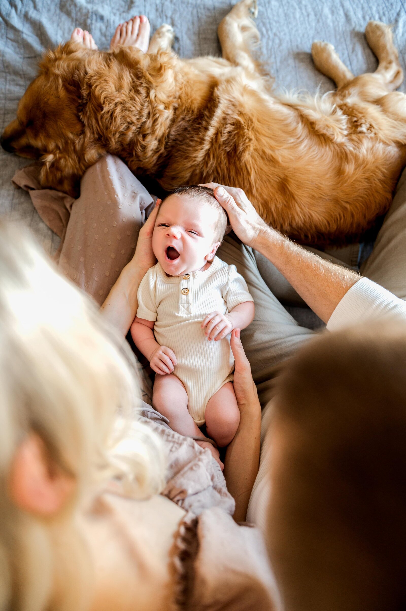 newborn baby boy yawning while parents hold him and dog sleeps