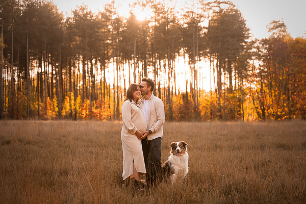 Een aanstaande moeder en haar partner poseren liefdevol met hun hond tijdens een zwangerschapsshoot, een intiem moment vol warmte en verwachting
