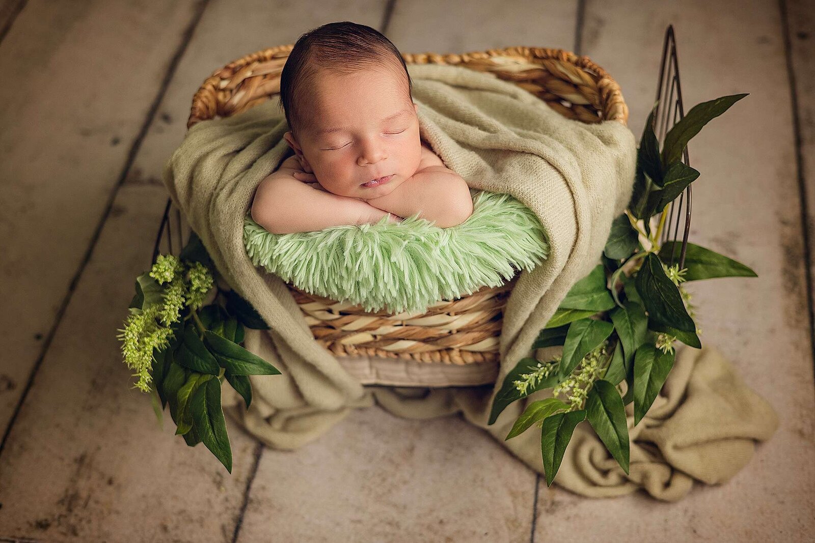 A tranquil newborn boy rests in a wicker basket, beautifully photographed by Bia Schaefer during an in-home session in Orlando.