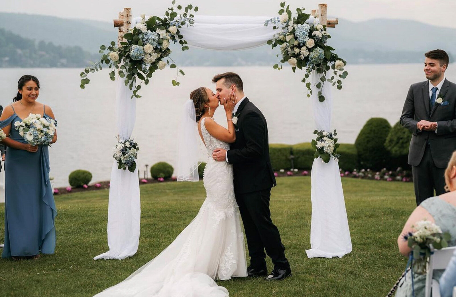 bride and groom share a kiss under a beautifully decorated wedding arch by a lakeside