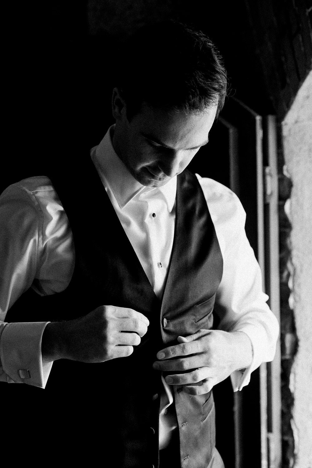 groom butttoning vest by window