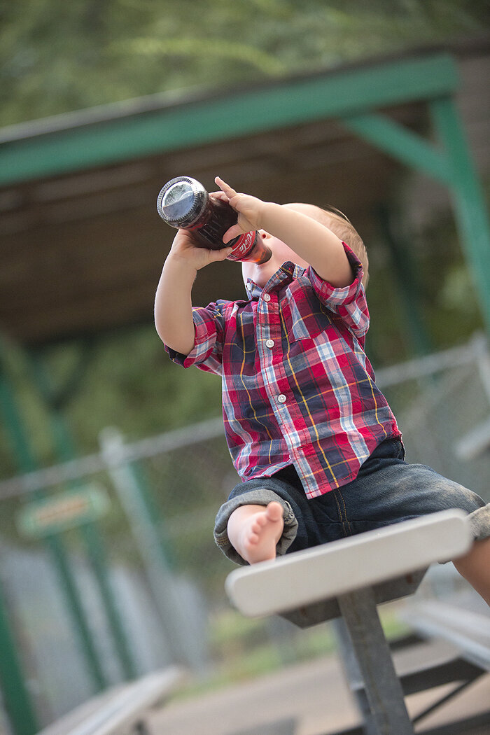 Toddler drink Coke at baseball field.