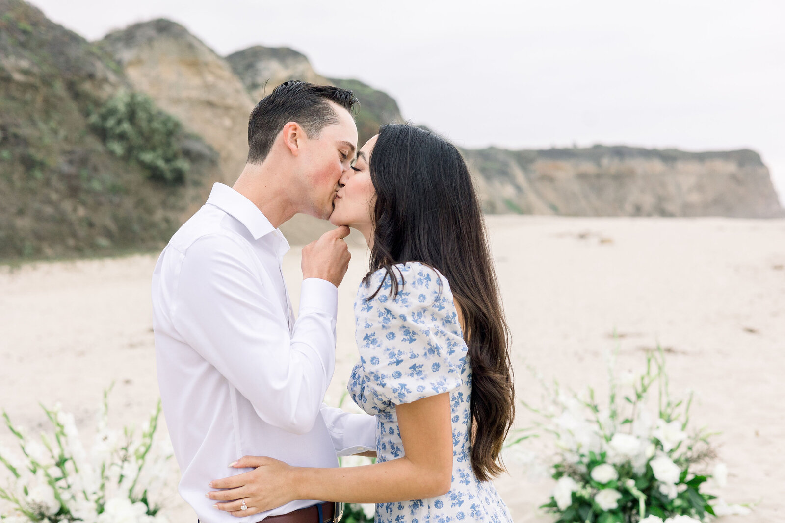 wedding photographer bay area captured candid proposal pictures with man and woman kissing at a proposal set up with white flowers and greenery