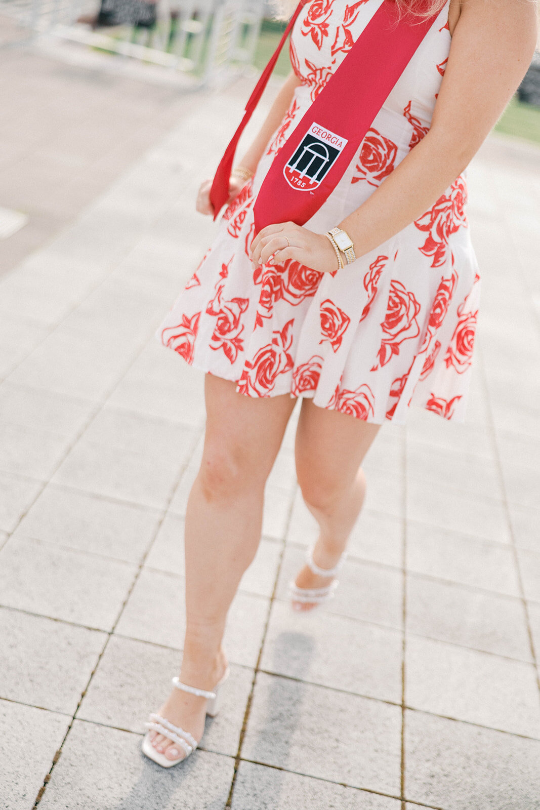 Girl walks in red flower dress with red sash with UGA's arch emblem 