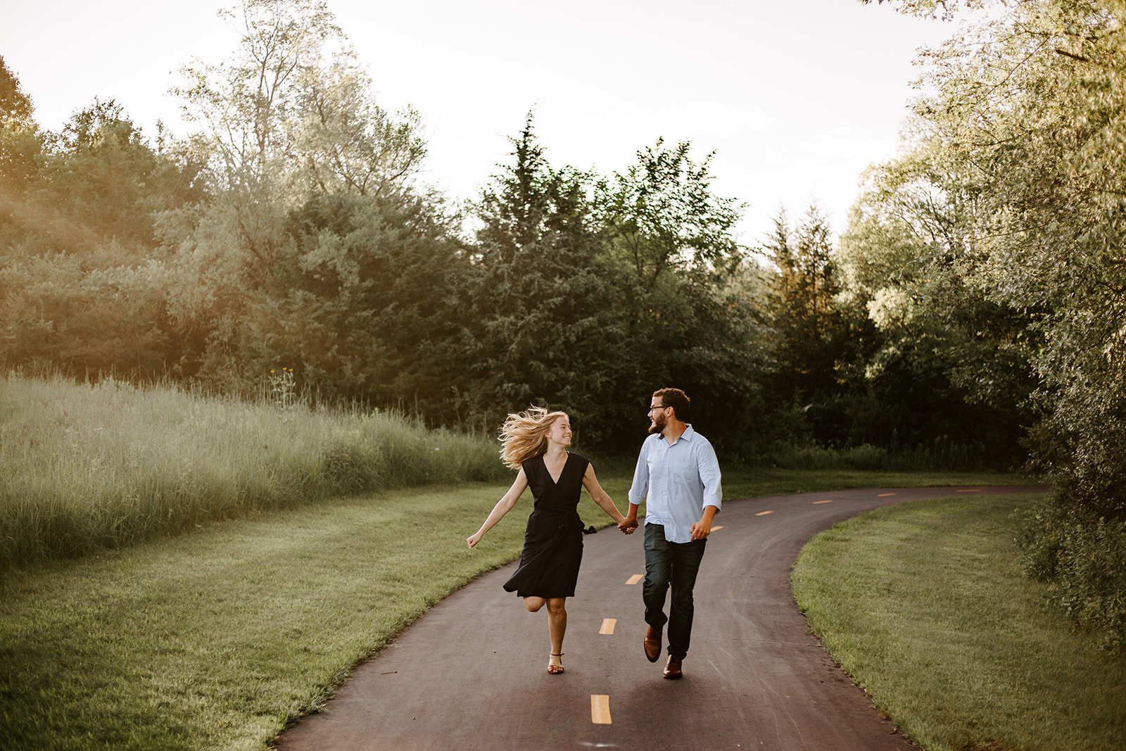 A couple holding hands running down a path in their engagement session