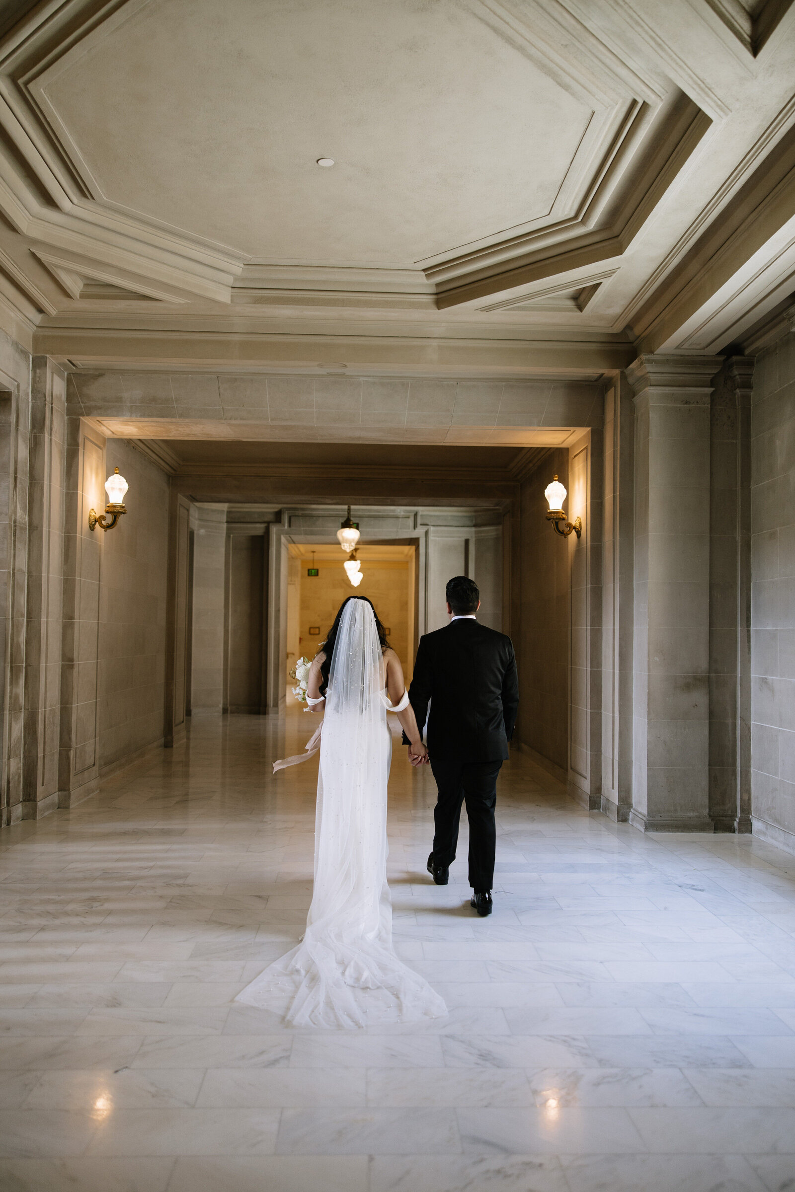 Bride and groom walk hand in hand through San Francisco City Hall during bridal portrait session