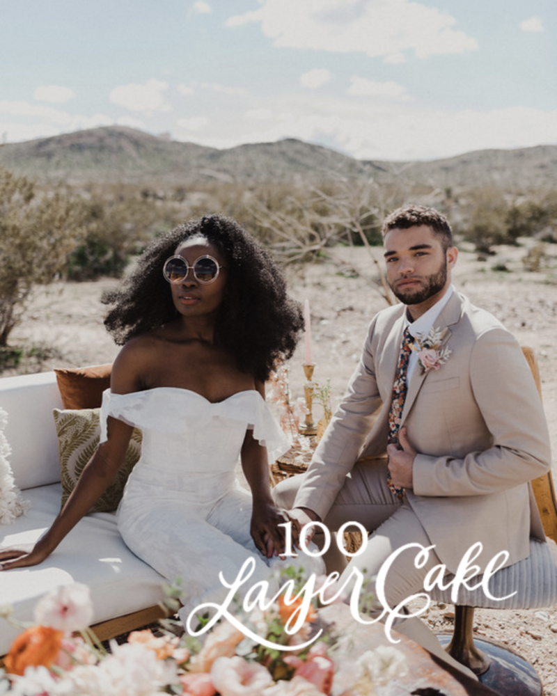 Kohnur modern boho bride in an off-shoulder jumpsuit with natural makeup and voluminous hair with groom in desert landscape featured on 100 Layer Cake.