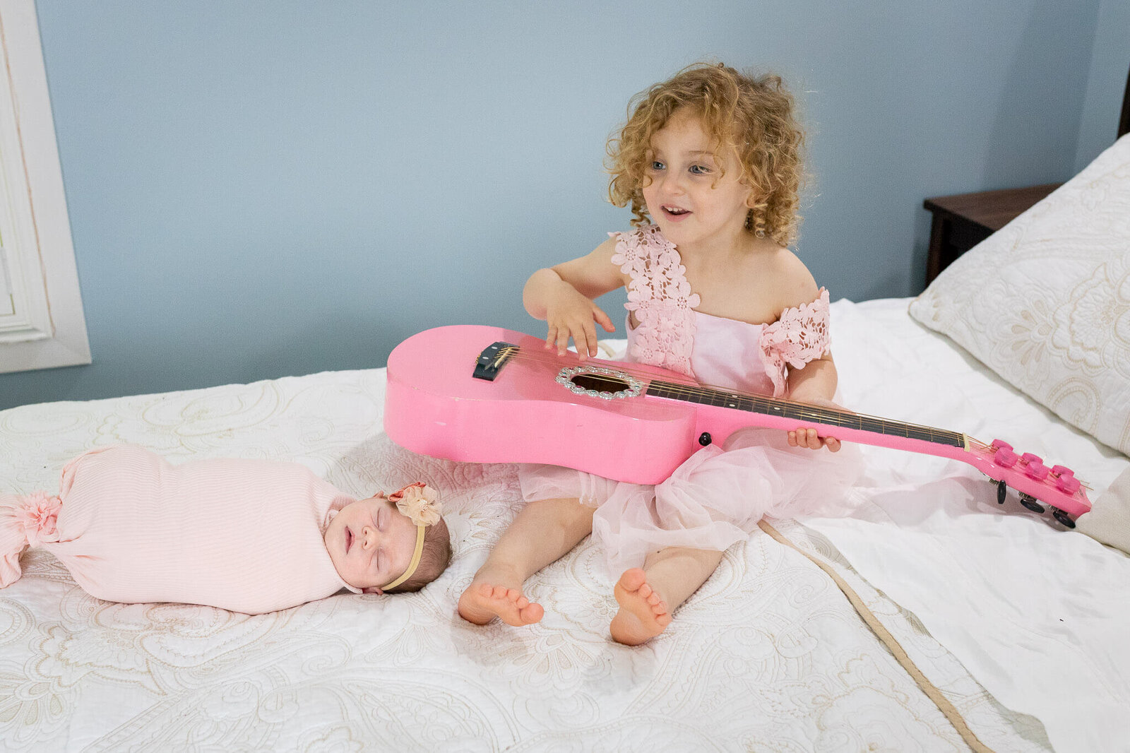 Big sister playing her pink guitar next to her newborn sister during their Alexandria newborn session.