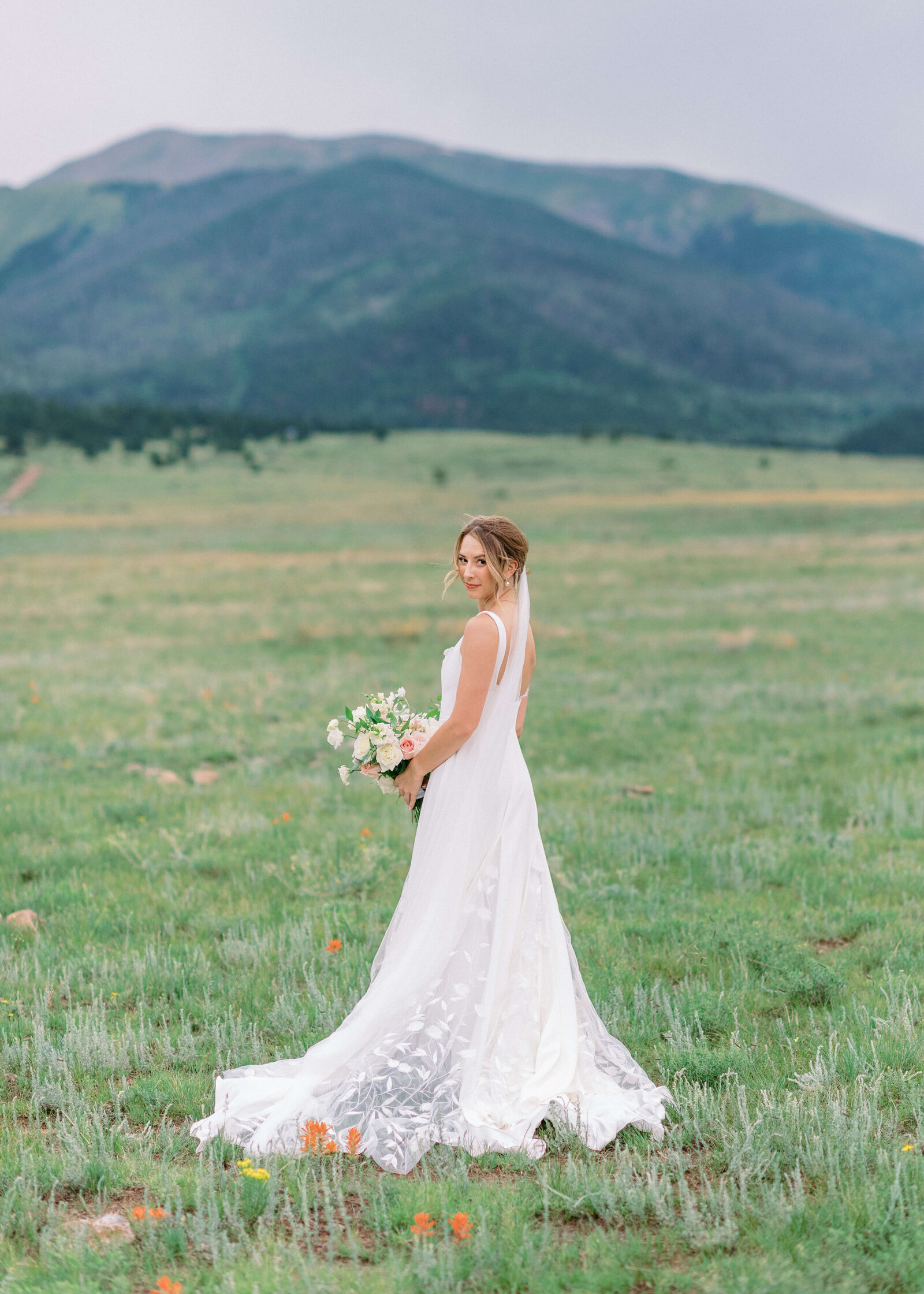 Beautiful bride stands in a field of wildflowers and grins at the camera