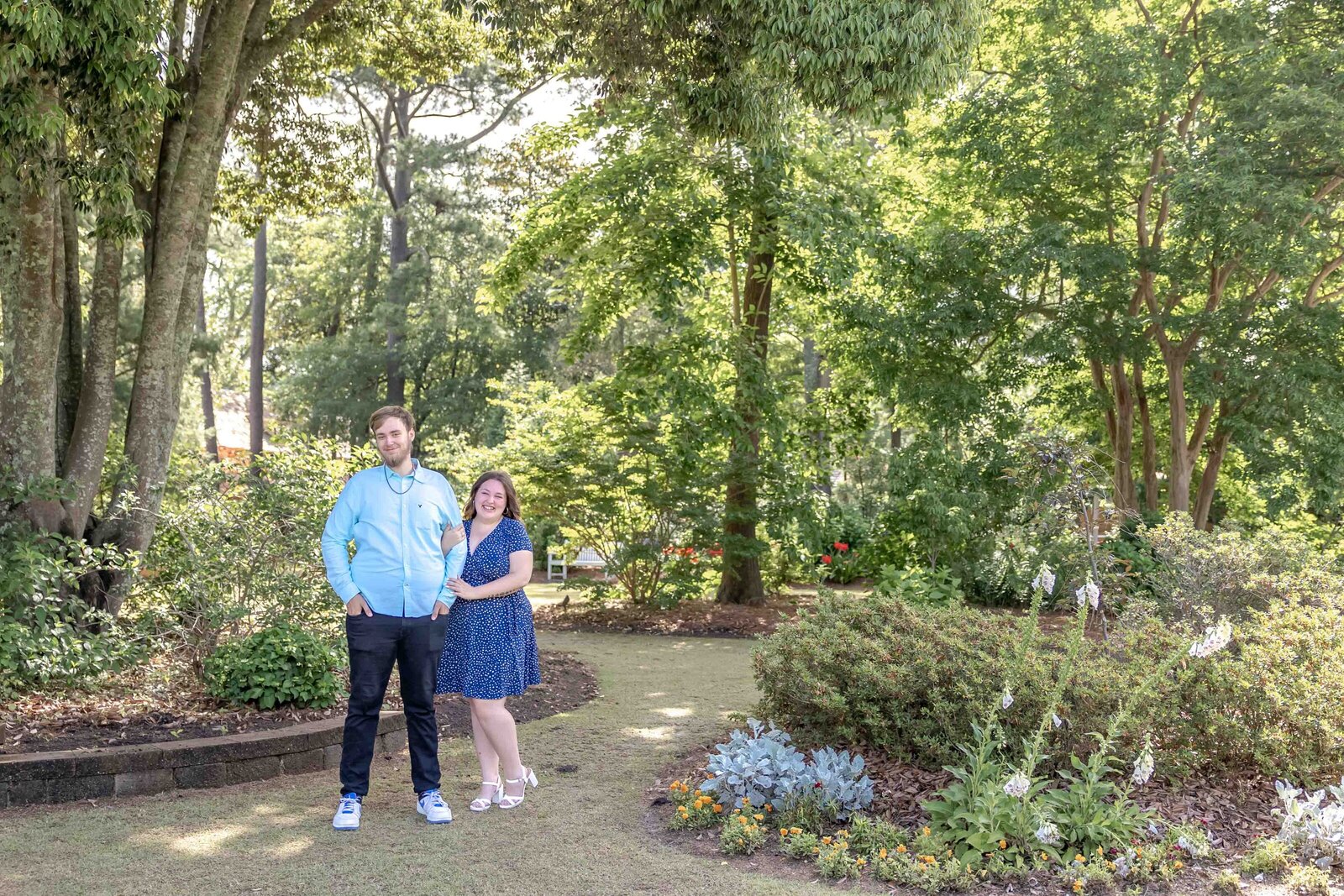 A couple playfully posing in a vibrant NC Arboretum garden in Wilmington, NC, surrounded by lush greenery and colorful flowers. This setting embodies the charm of artistic wedding photography, appealing to couples seeking affordable wedding photography in Wilmington.