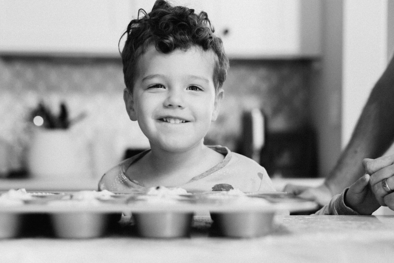 Little boy smiles over a full pan of muffins