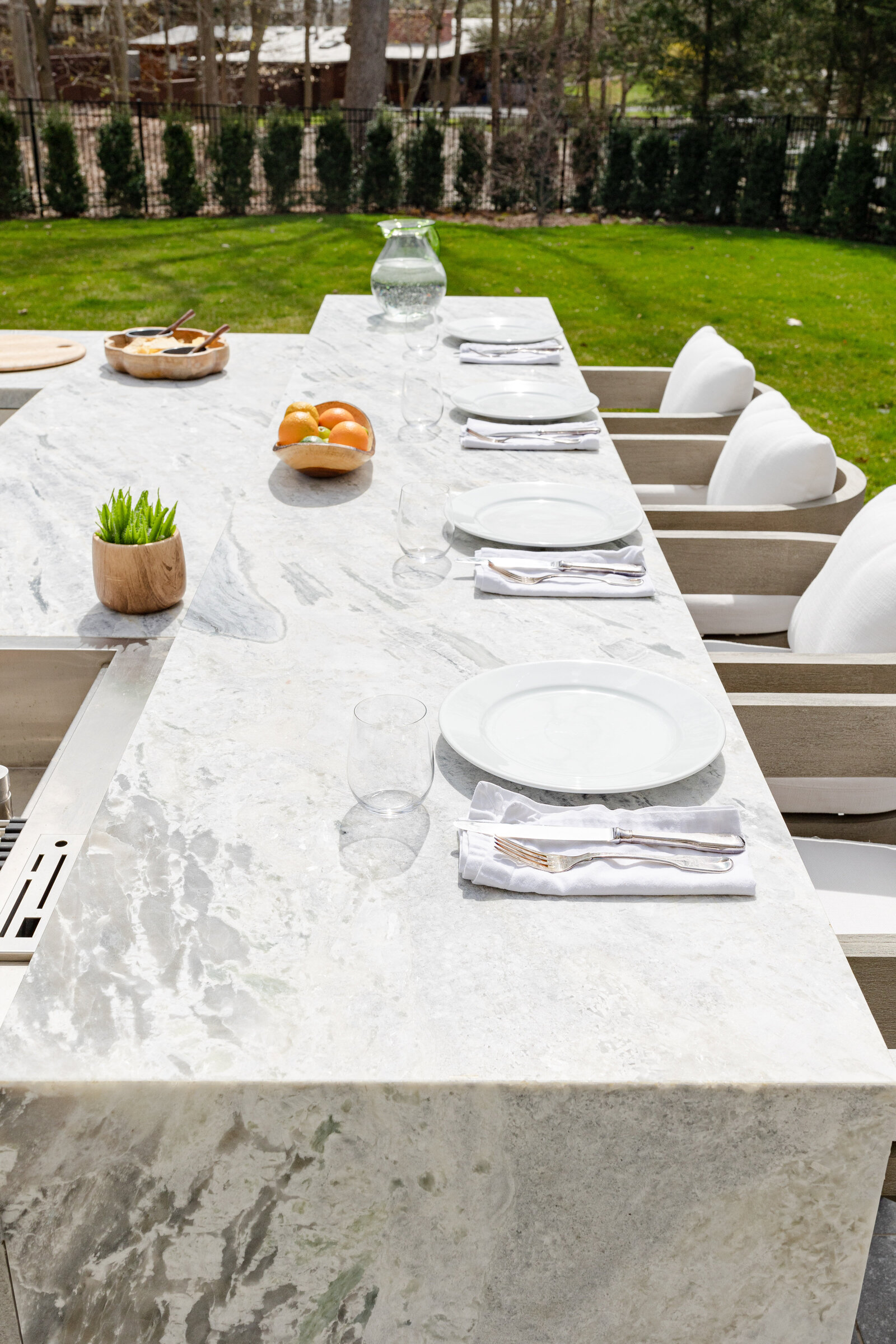 The outdoor kitchen features a stone bar, table setting, and decor, with a Princess White Quartzite finish.