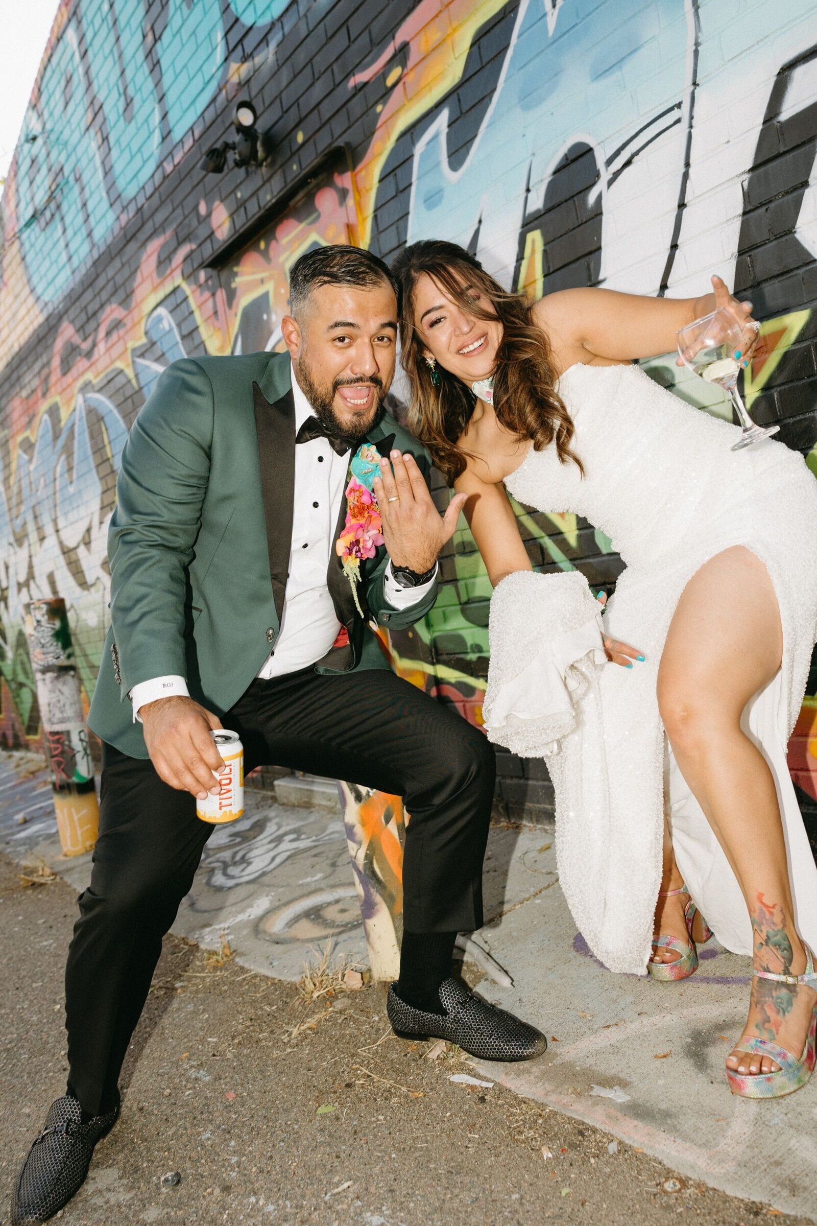 A bride and groom stand in a city alley full of graffiti