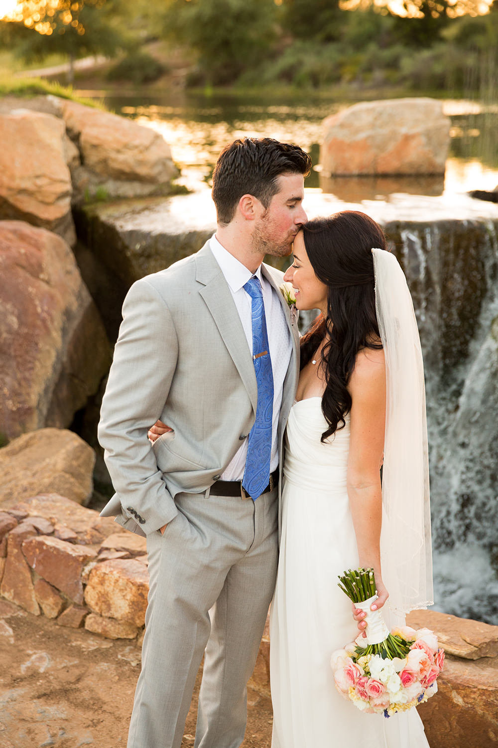 groom kissing forehead by waterfall