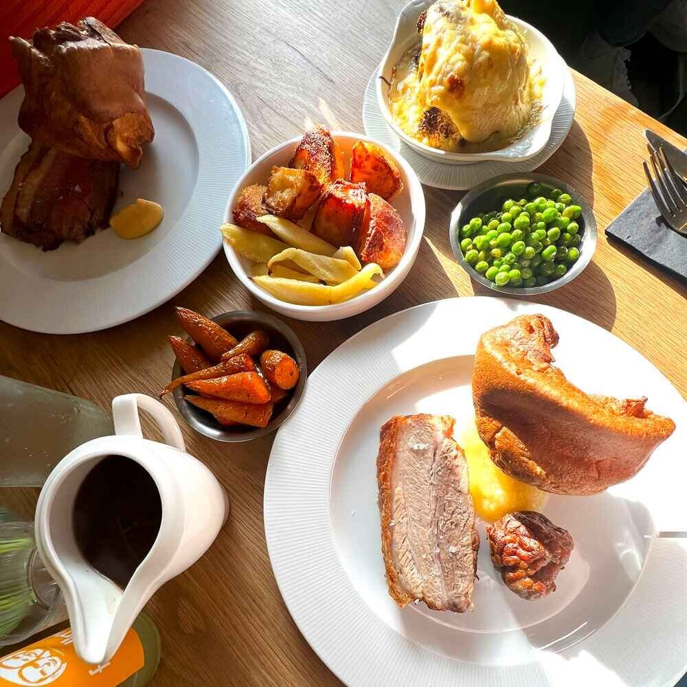 A roast dinner on separate places, gravy jug, meat, yorkshire pudding and mixed vegetables