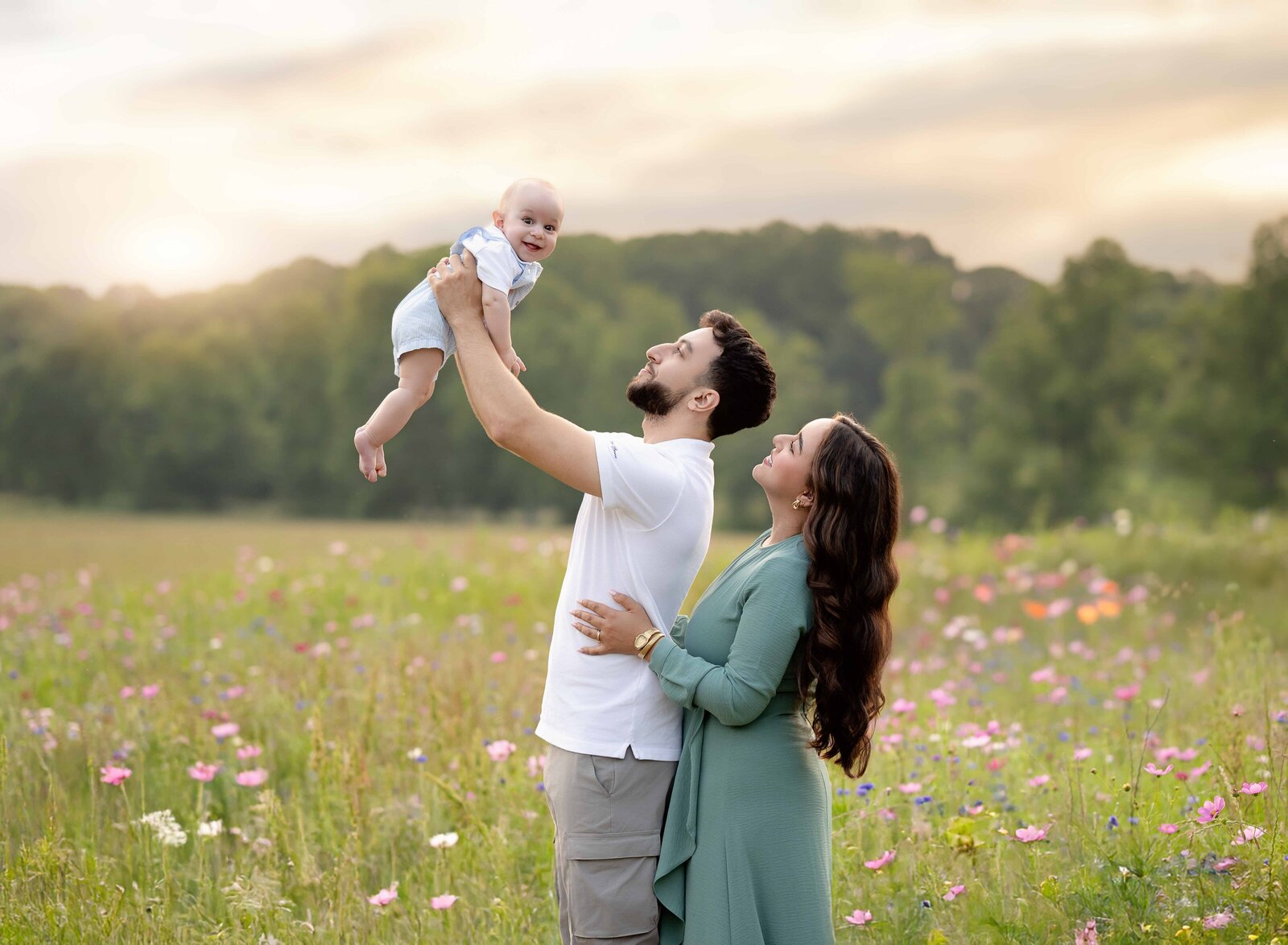 Dad holding baby in air and Mom hugging Dad and smiling at baby. Atlanta Photographer, Jenni Nikki, photographed this image in Lawrenceville, GA.