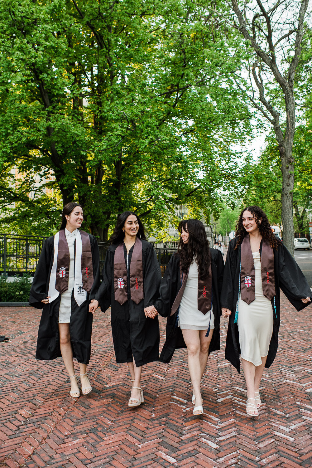 grad girls walk down street in robes and sashes