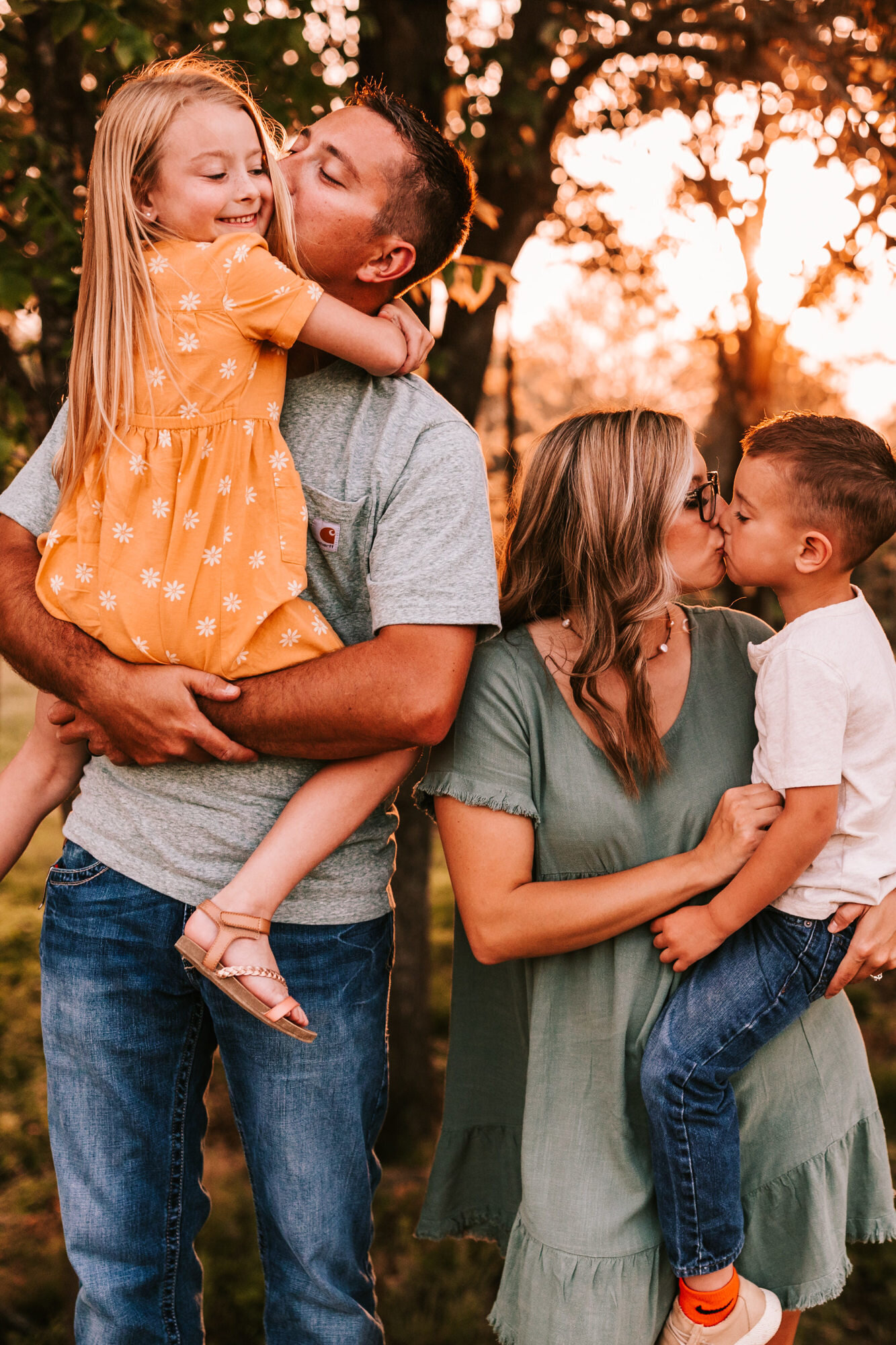 family of four with husband kissing daughter on the cheek and wife kissing son on the lips family