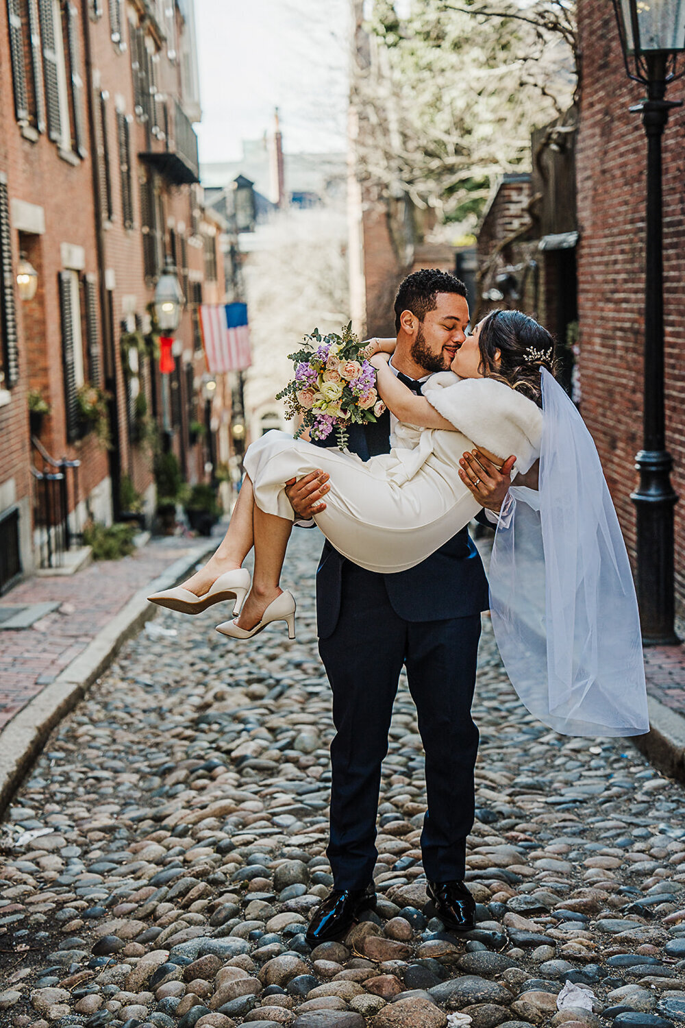 groom carries bride on acorn street in boston elopement
