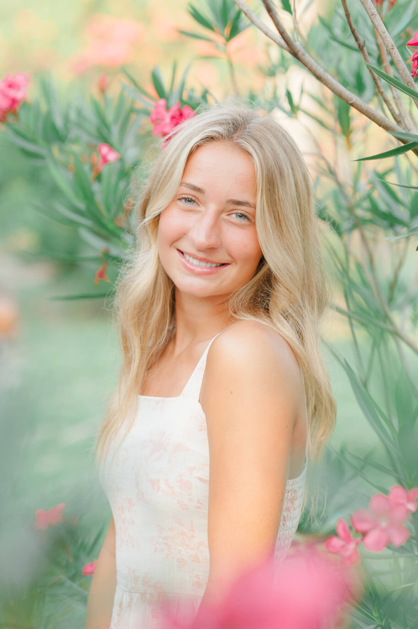 Senior girl stands in the midst of beautiful pink florals near the beach for her senior photo session