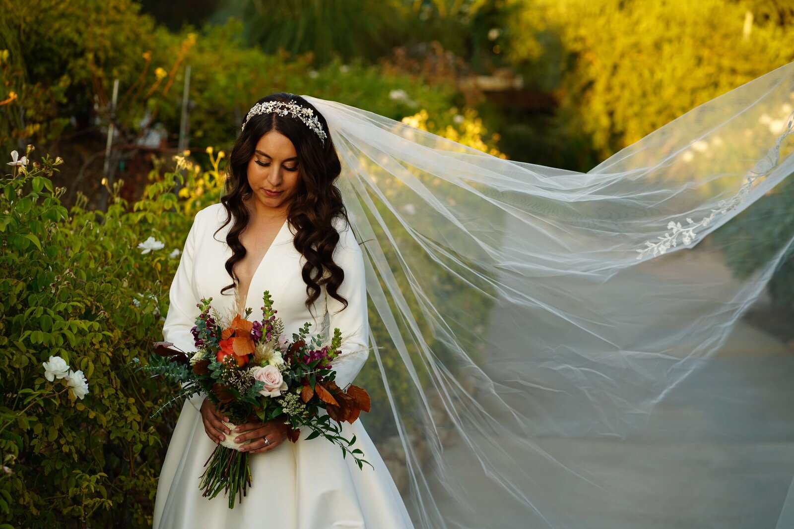 Weddings and Family Portraits in Orange County bride holding floral bouquet and veil blowing in the wind