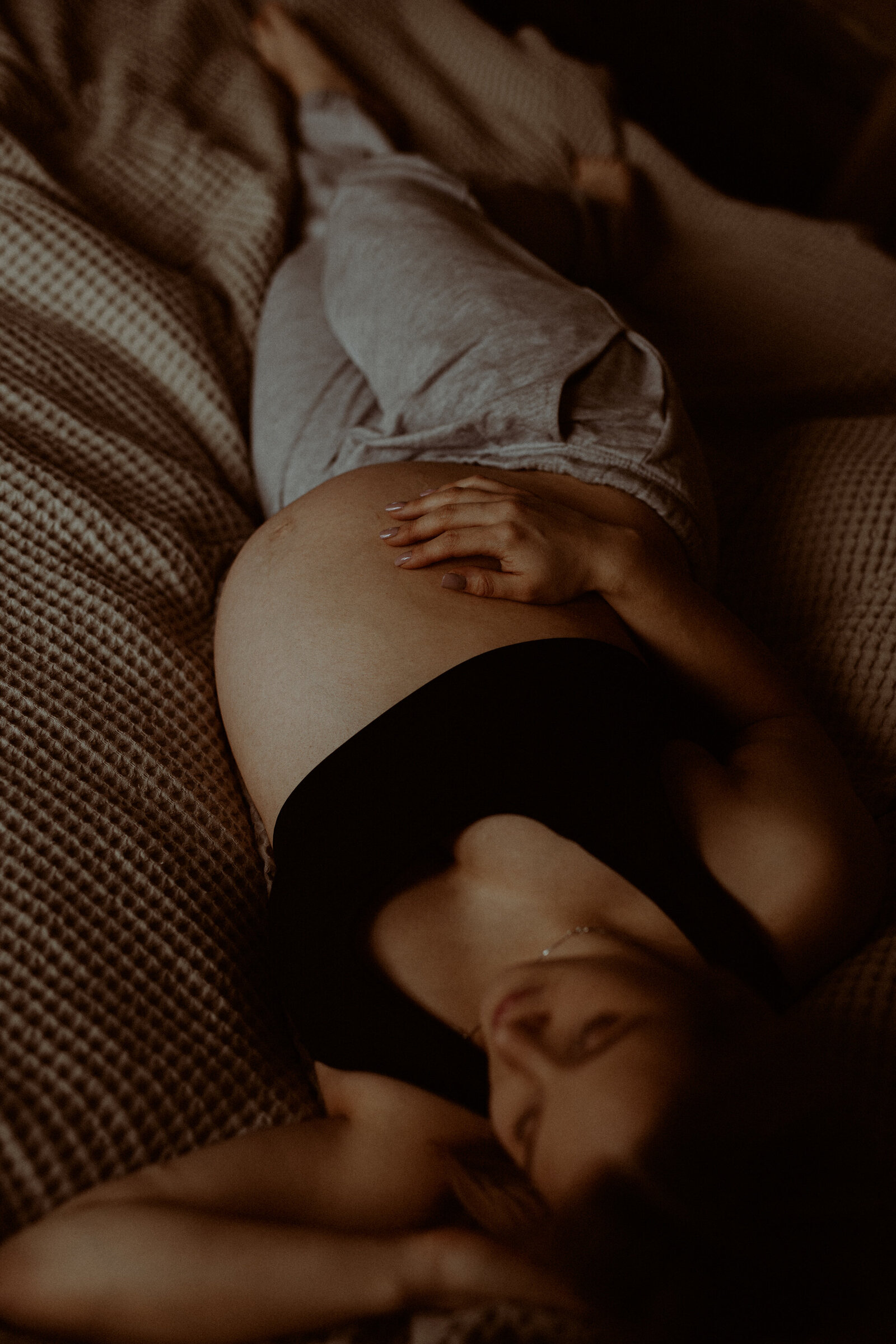 en gravid mamma i mjukisbyxor och bh ligger på en säng