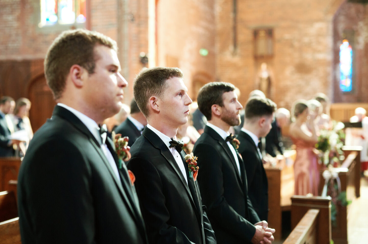 Groomsmen standing during the wedding ceremony inside a large catholic church