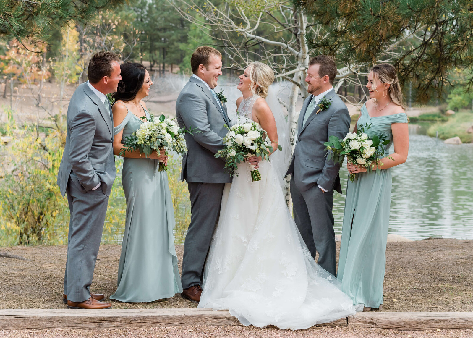 A bridal party stands together in front of a Virginia fountain and laugh together