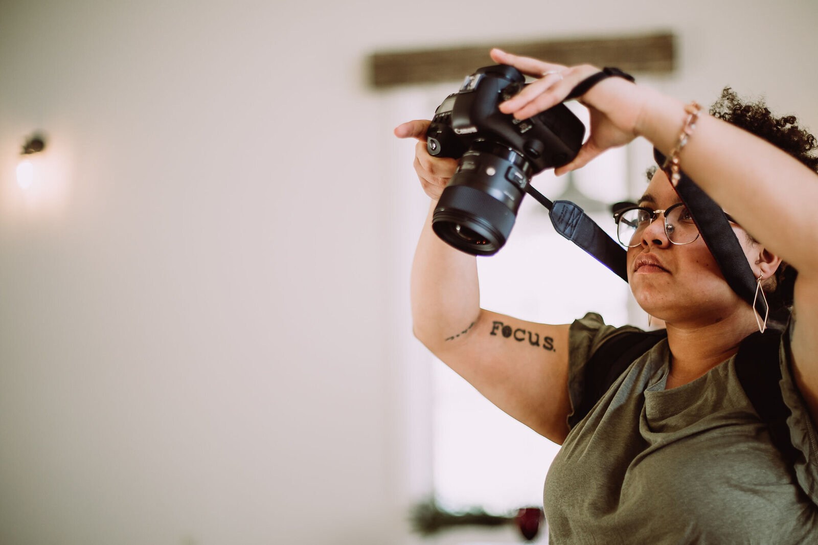 Photographer holding camera arm tattoo white walls green shirt