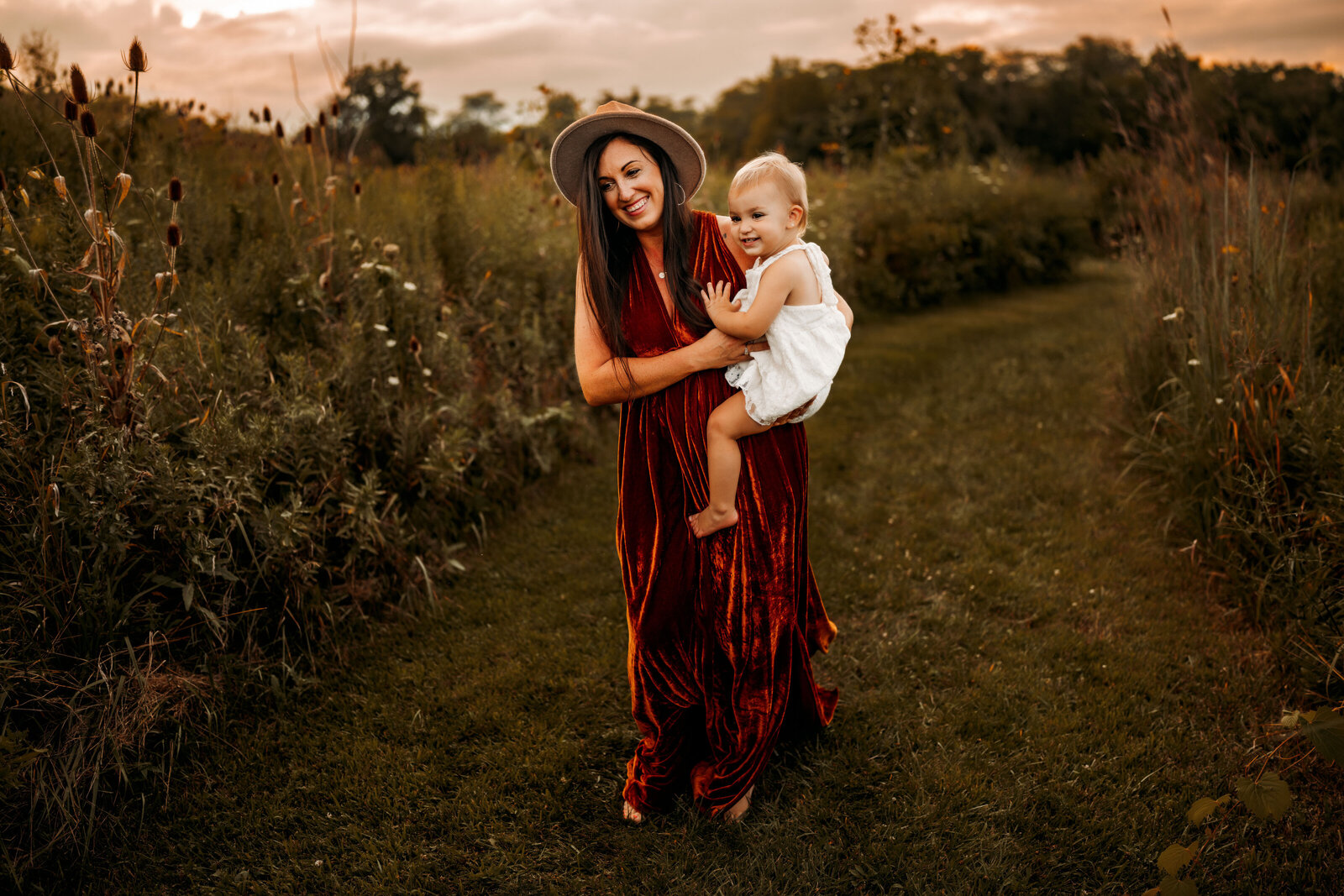 Mother holds daughter while walking through a grassy trail